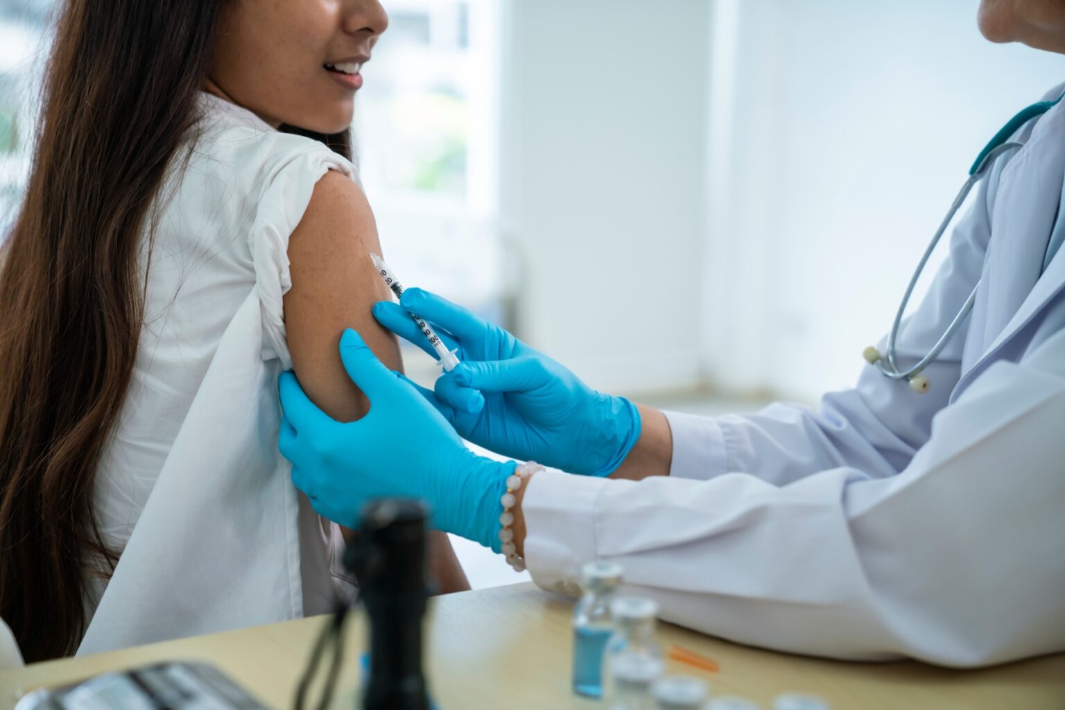 Girl gets a vaccination in her arm, nurse or doctor wears teal-colored medical gloves