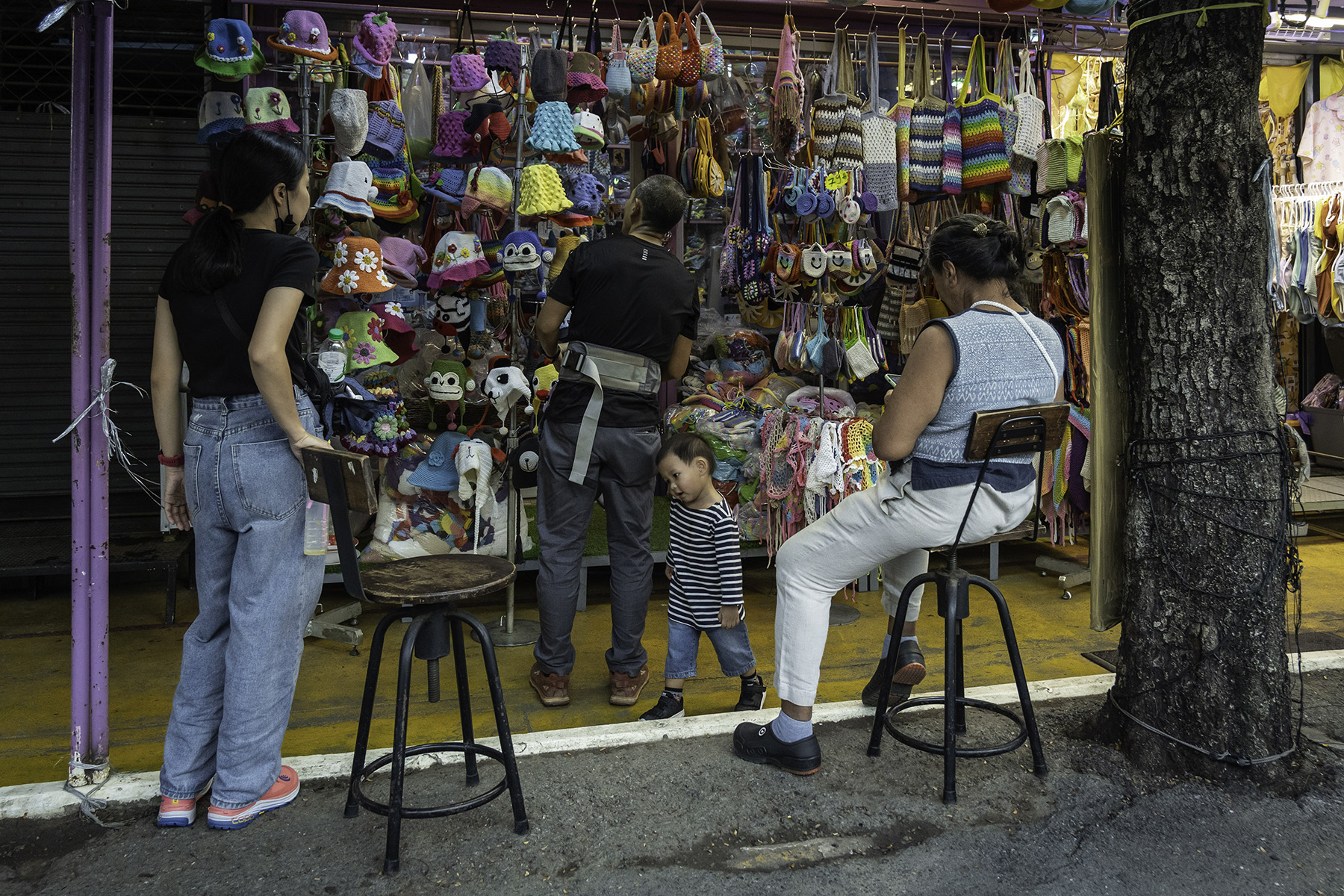 A vender sits at his stall with a child and a woman standing nearby at Chatuchak Weekend Market