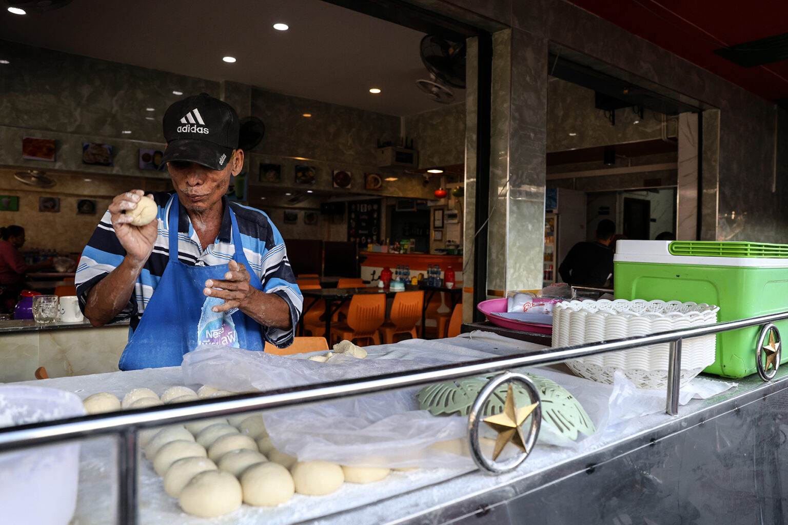 A market vendor stands behind his food counter rolling some kind of dough in his hand in Thailand