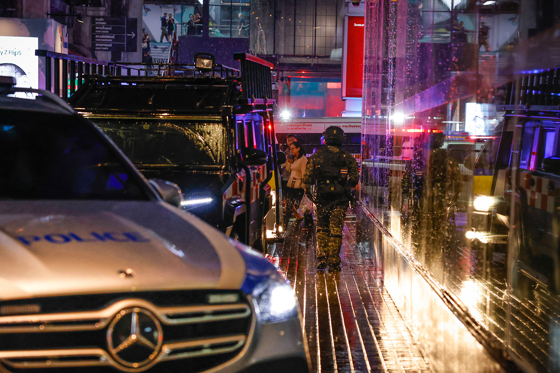 Night time, police vehicle in front, armed police officer walks away towards Bangkok Mall