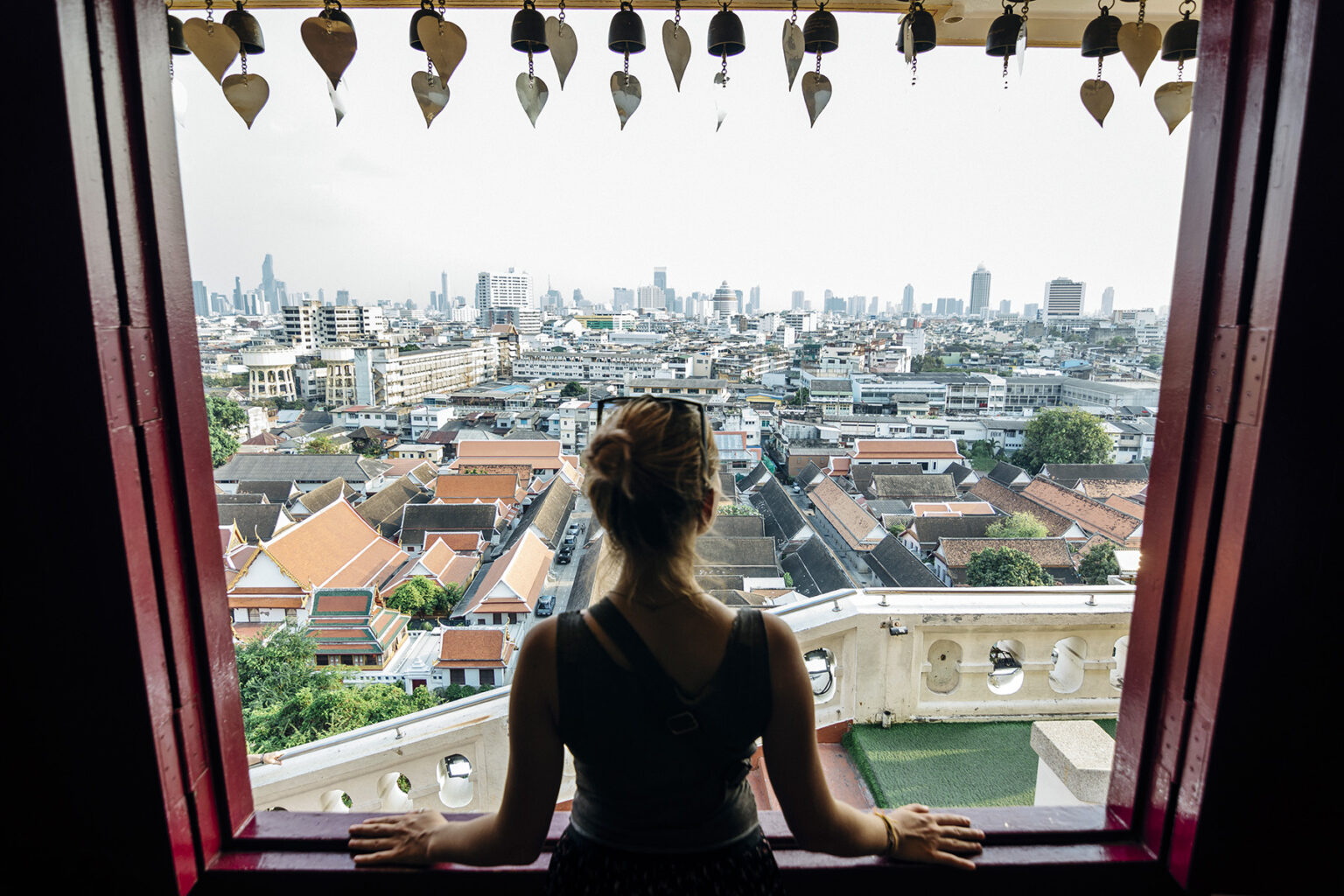 Woman looking out of the window of a hotel onto the cityscape of Bangkok, Thailand's capital.