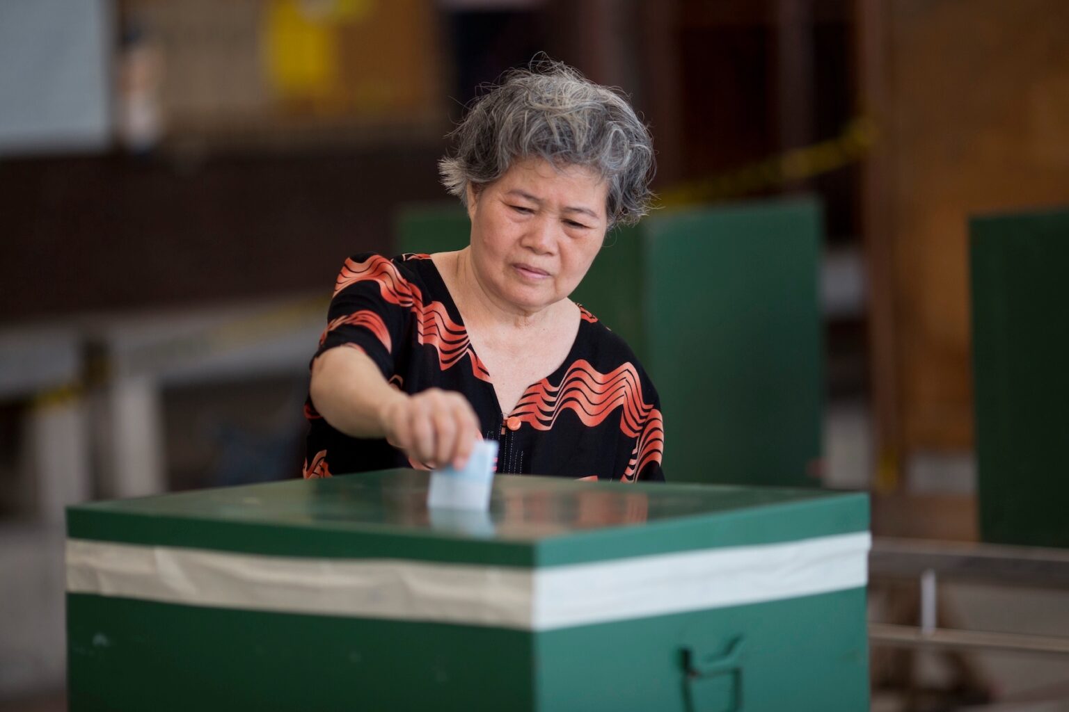 An older Thai woman casts her vote with a paper ballot during an election