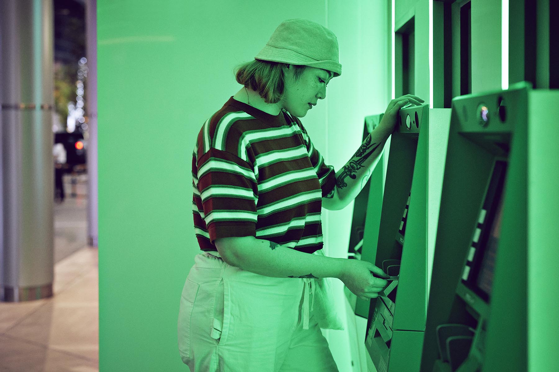 Woman wearing striped T-shirt using ATM. The bank is giving off a green glow.