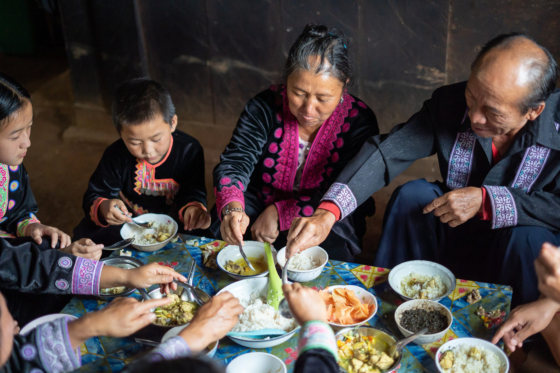 Family in traditional Hmong clothing sitting around a table and sharing a meal in Chiang Mai, Thailand.