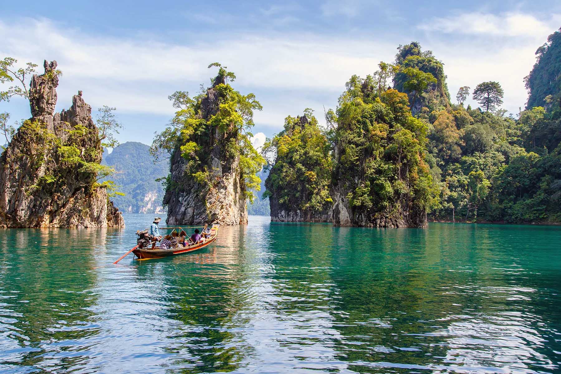 A small boat with tourists sails a lake in the Khao Sok National Park, where emerald waters and small islands are some of its main attractions.