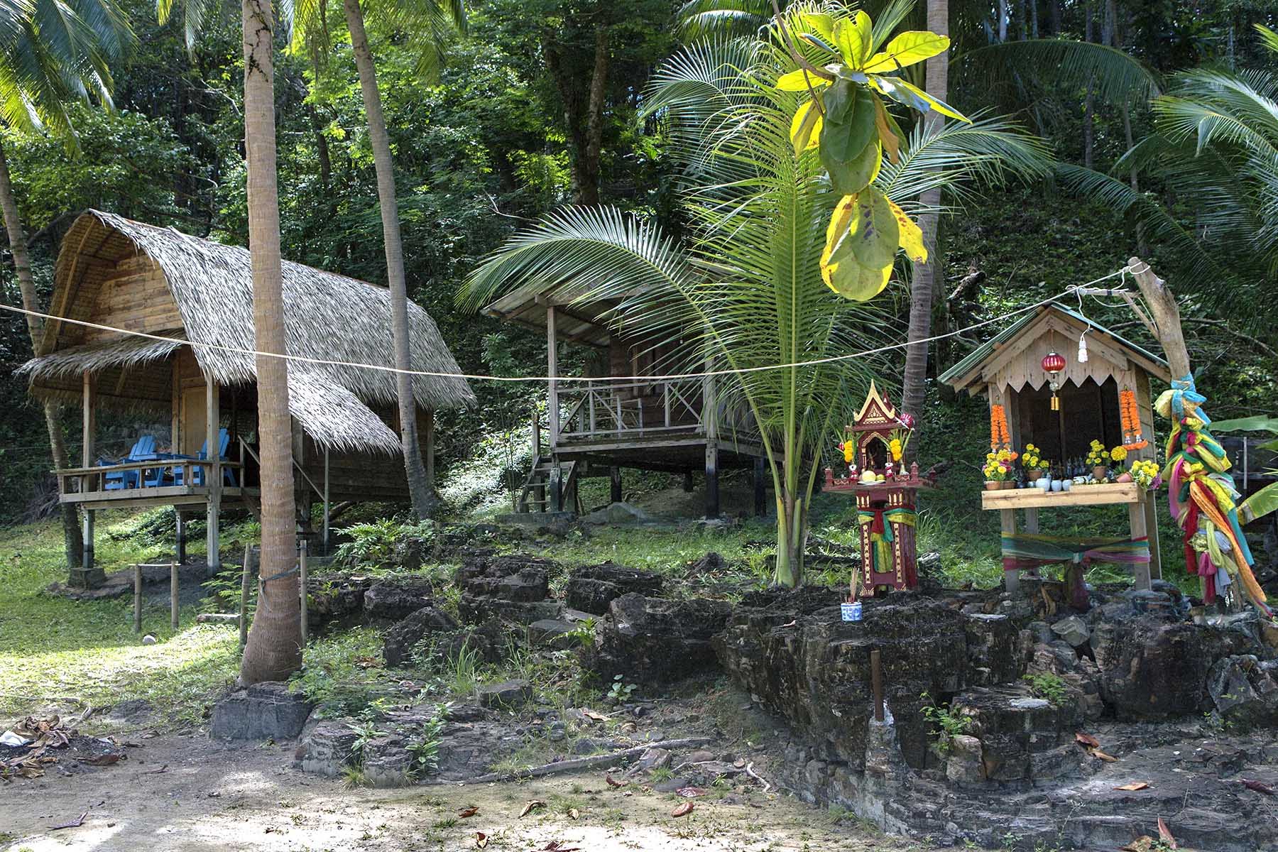 Small spirit houses with offerings and flowers stand next to big huts on the beach on Koh Wai island in eastern Thailand.