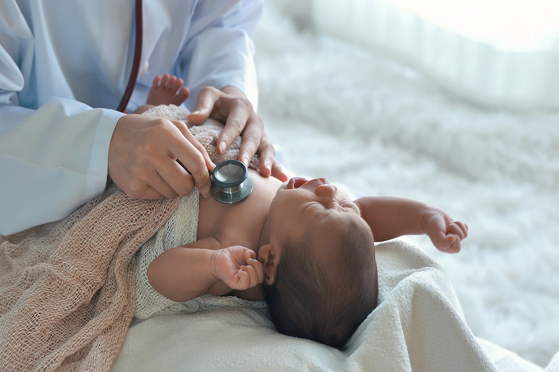 Hands of doctor hold a stethoscope on a small baby's chest - baby cries