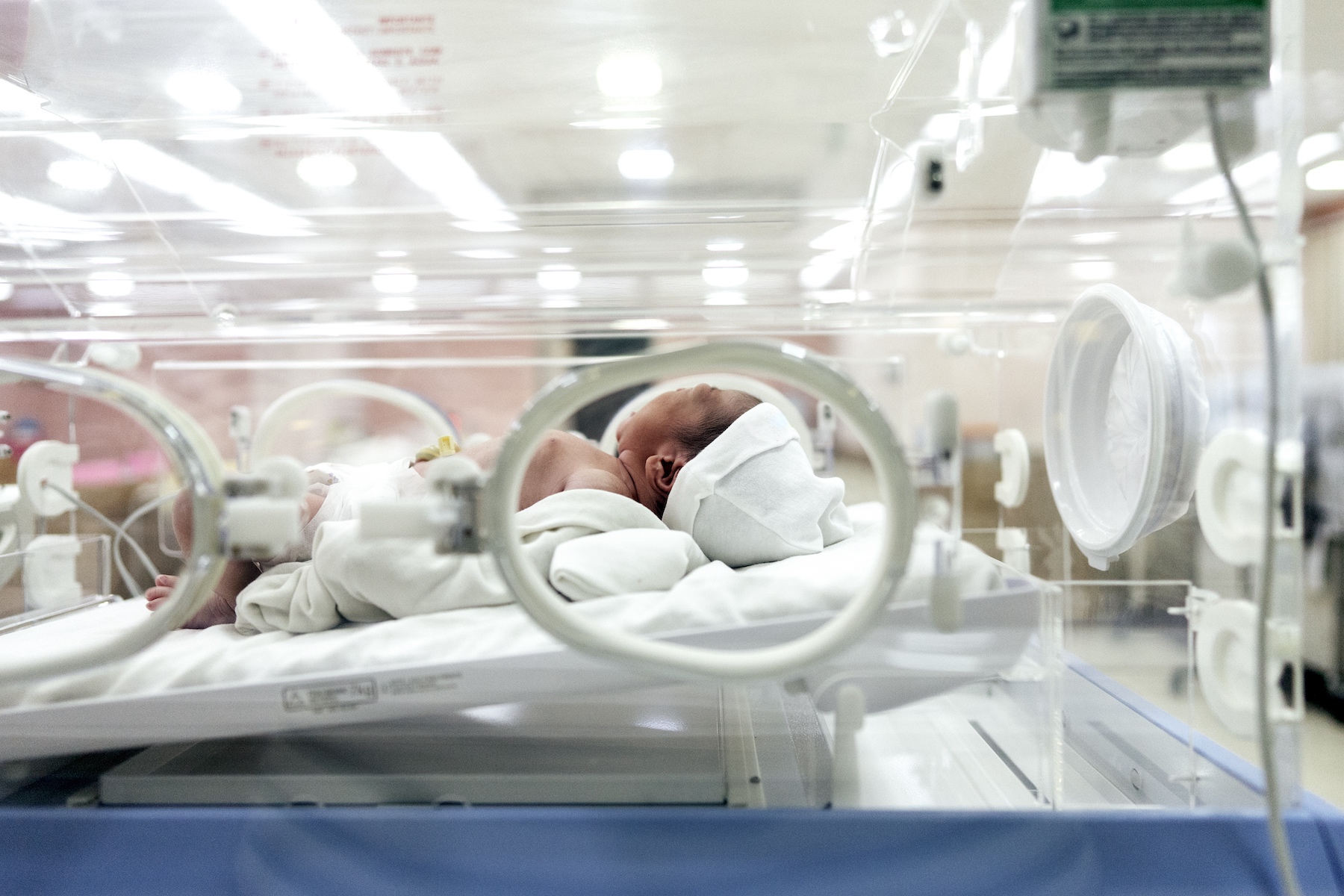 A small newborn baby cries while laying in a hospital incubator 
