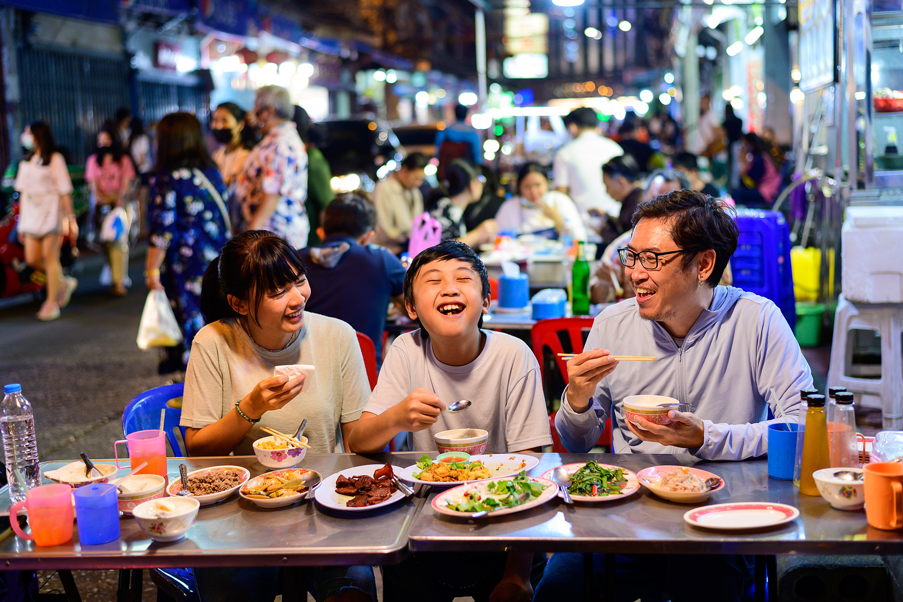 Family enjoy eating food on street food restaurant with crowd of people at Yaowarat Road, Bangkok