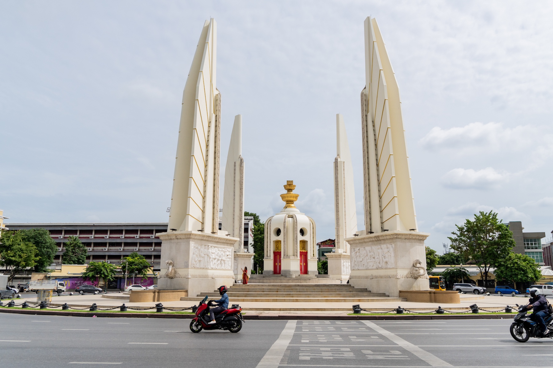 A view of the Democracy Monument in Bangkok, Thailand from across the street as motorcycles go by