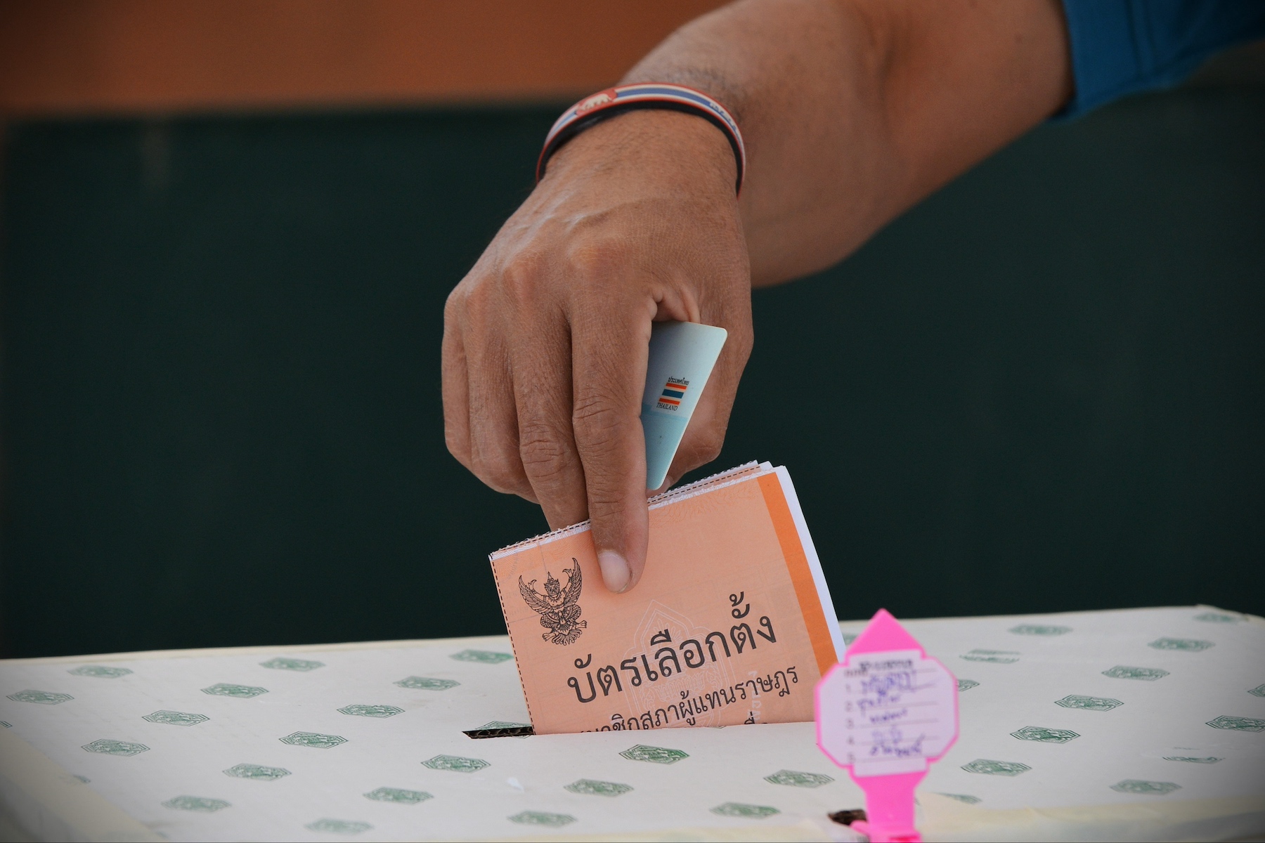 Close-up shot of a hand placing a paper ballot into a box during the Thai election