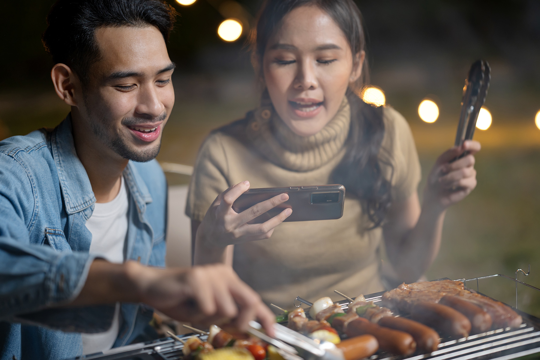 A couple barbecues, the woman films it on her mobile phone