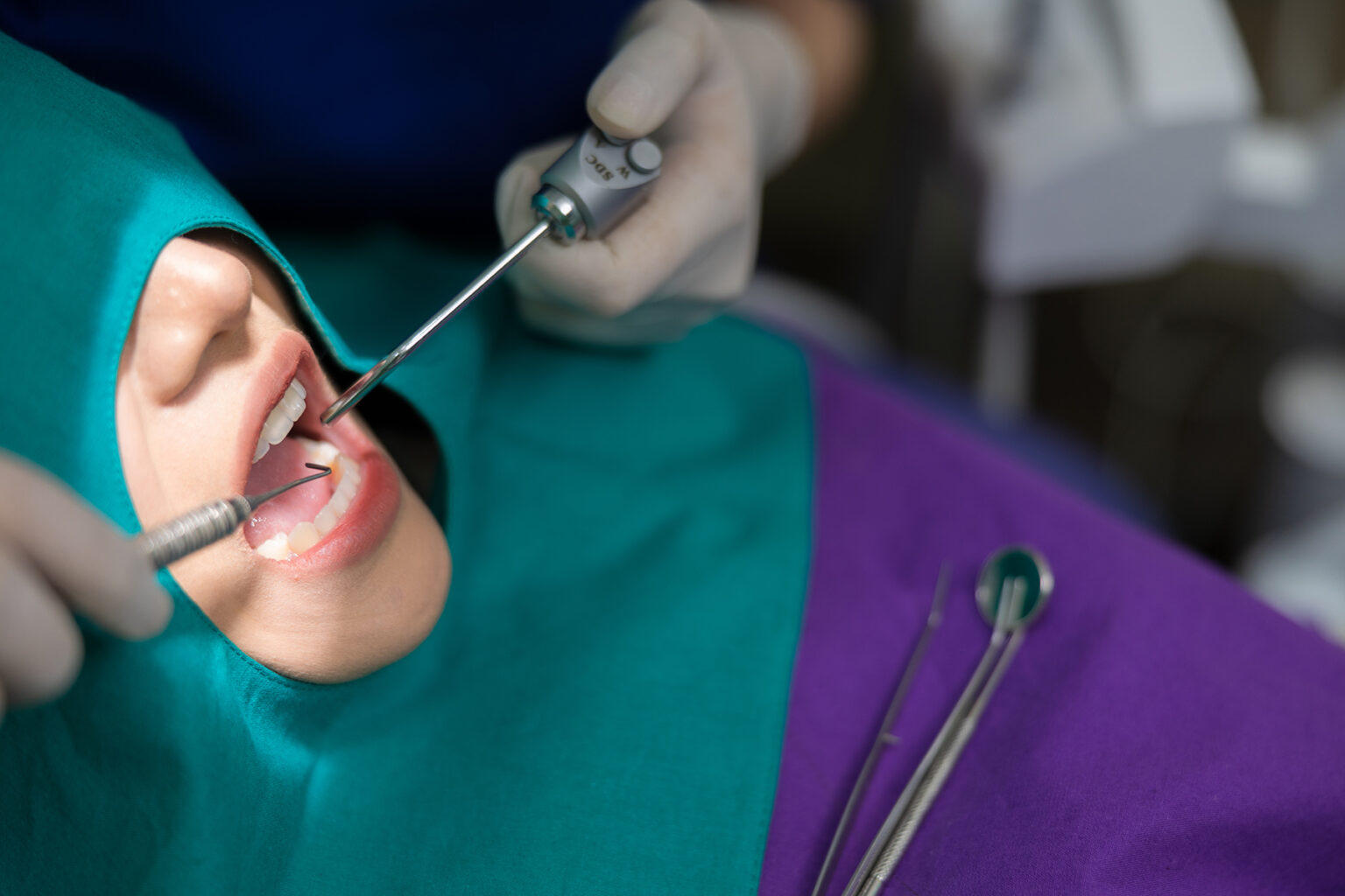 Close up of a dentist working on a patient's teeth - their face is covered with a green cloth with an opening for the mouth