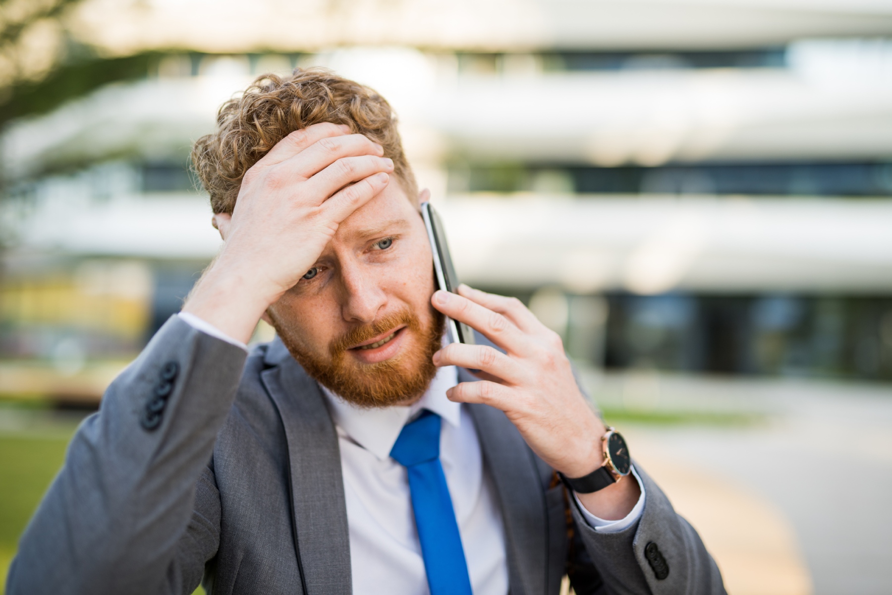 thailand emergency number: a red-headed business man in a suit speaking on his mobile phone and holding his hand to his head while looking anxious

