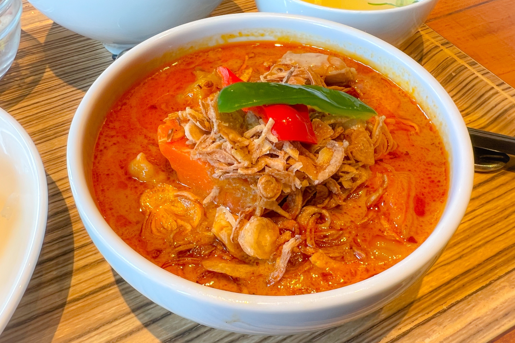 A full bowl of gaeng massaman gai topped with green and red peppers