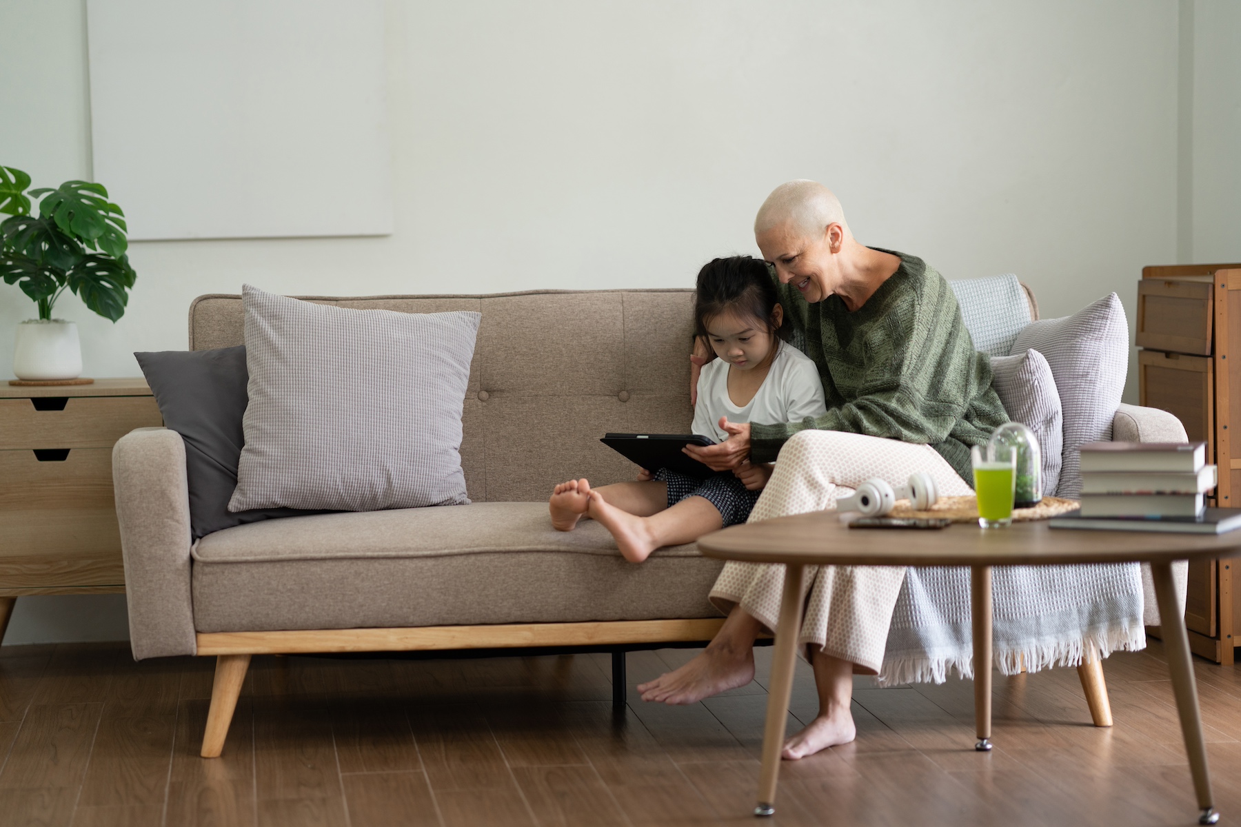 A grandmother and granddaughter sit on the sofa together looking at a tablet