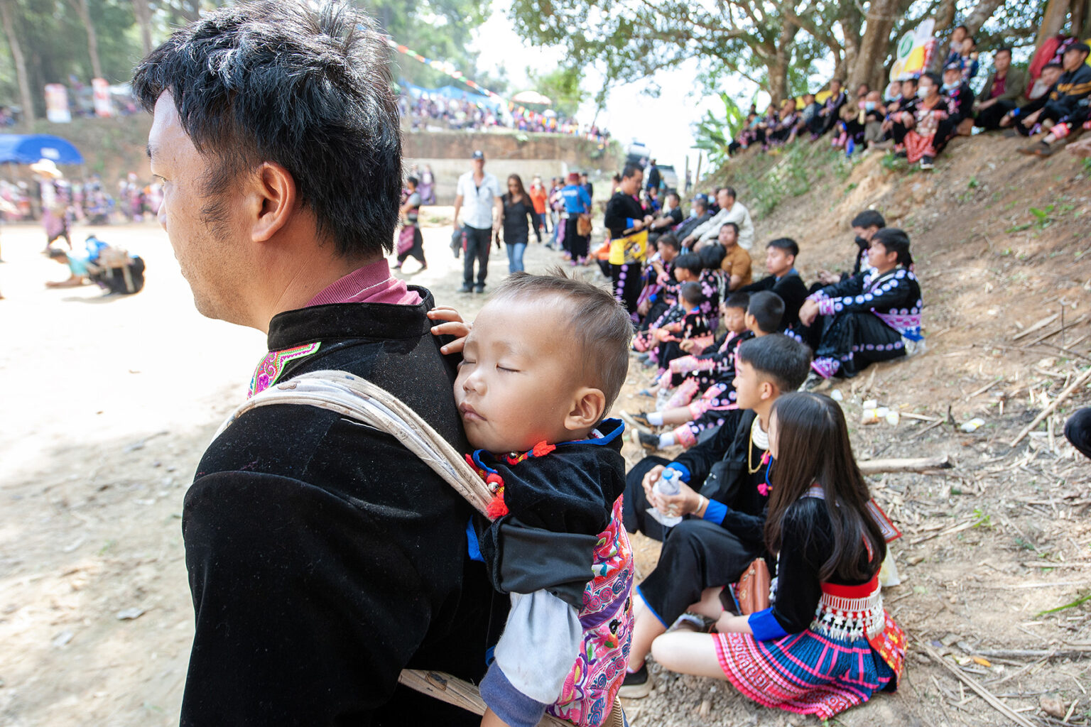 Hmong hill tribe man carries his sleeping baby on his back in a sling during the Hmong New Year celebrations.