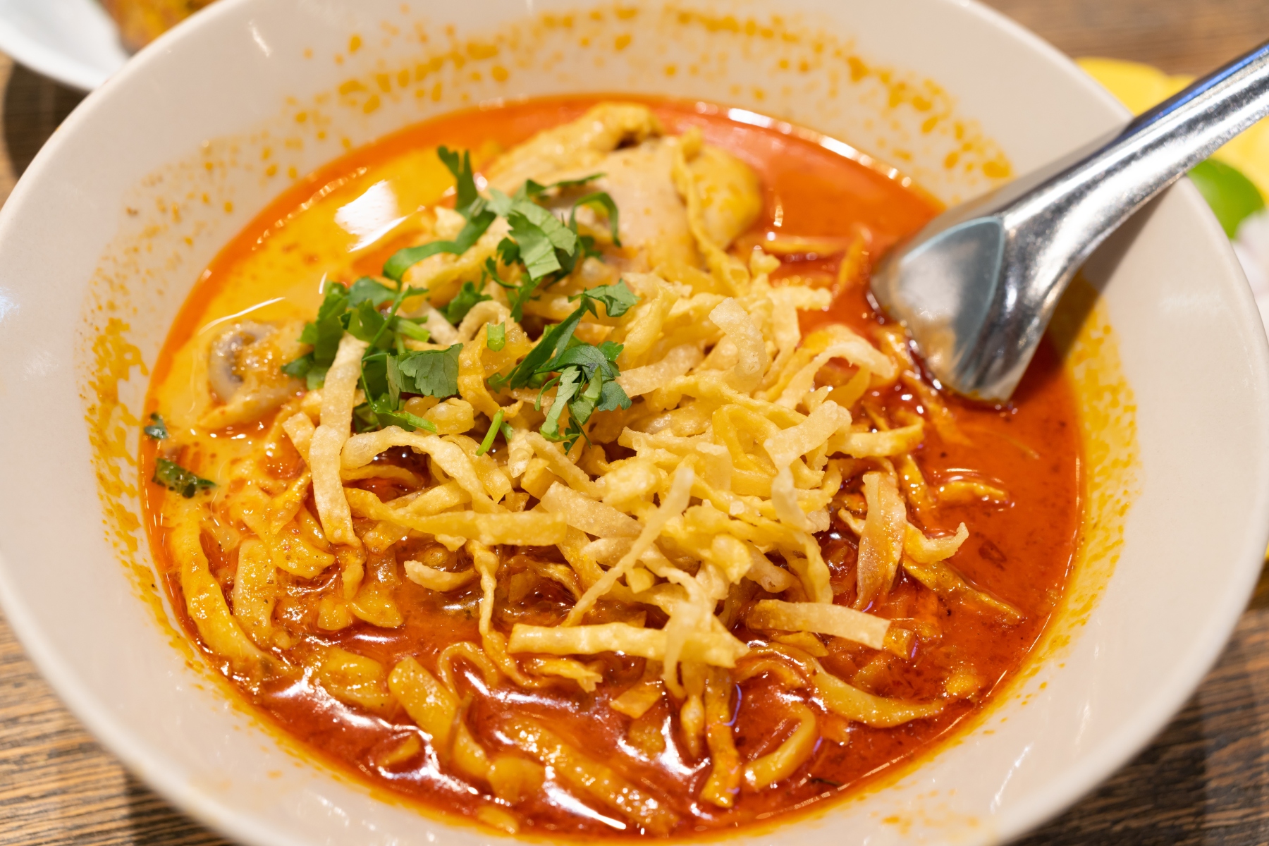 Close-up on khai soi, with a spoon dipping into the creamy red soup