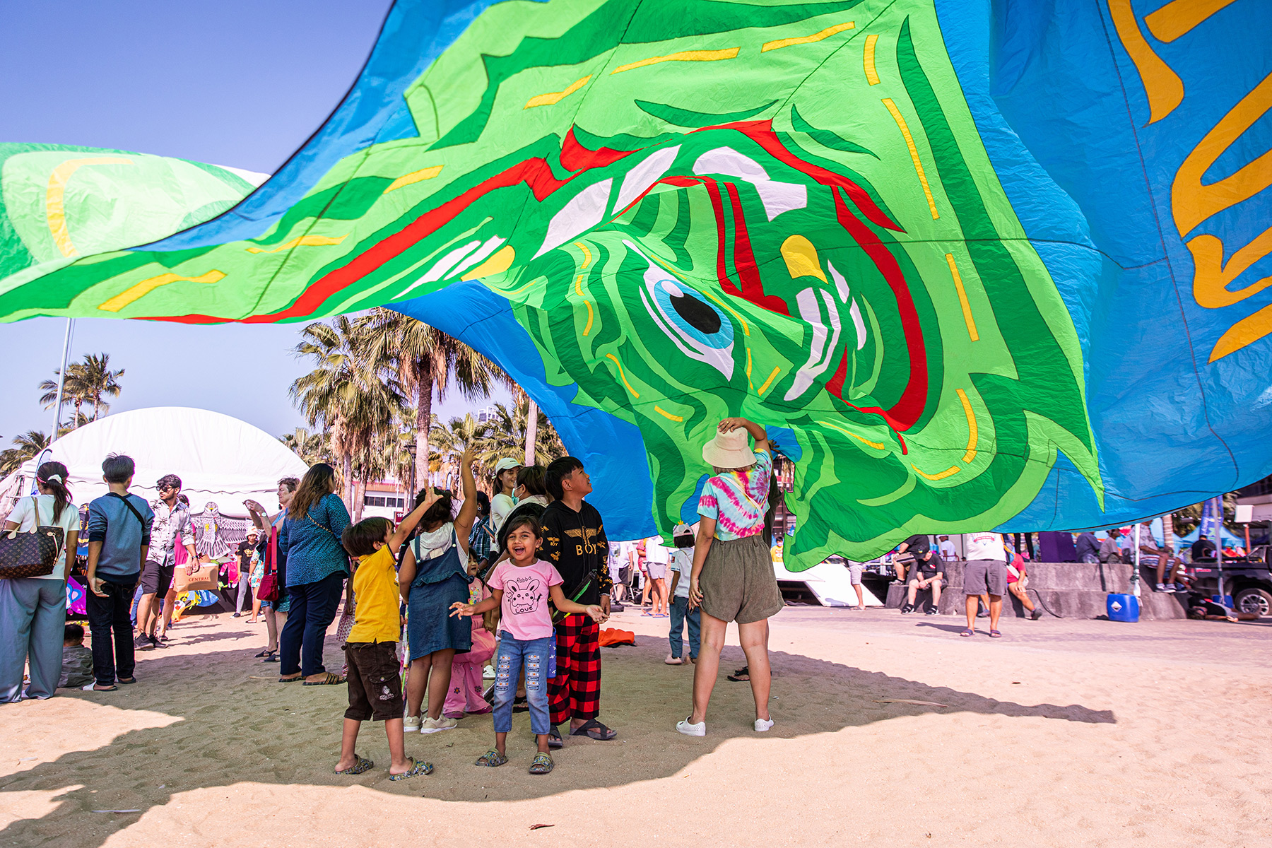 Children play under a large green kite on a sunny day