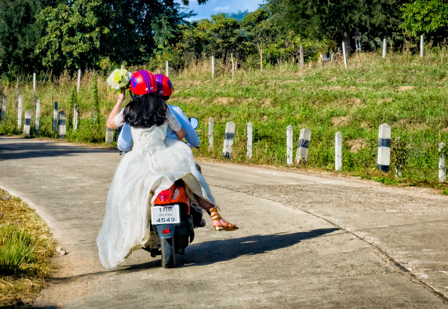A newlywed couple in their wedding attire ride a motorcycle away from the reception