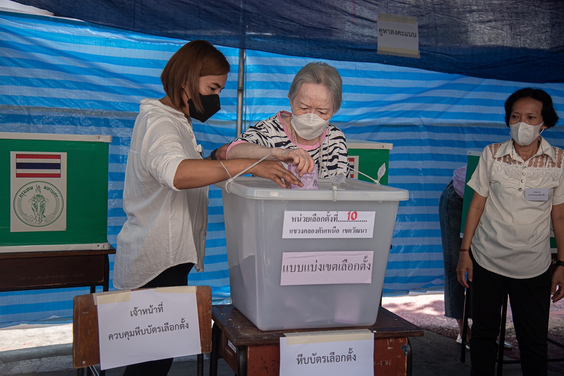 An older woman casts her vote in the Thai general election with help from polling staff