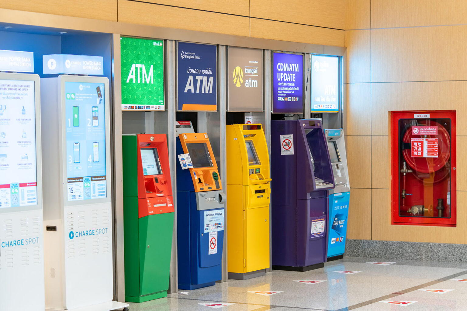 A row of four ATMS, green, blue, yellow, purple, and teal. The corridor is empty.