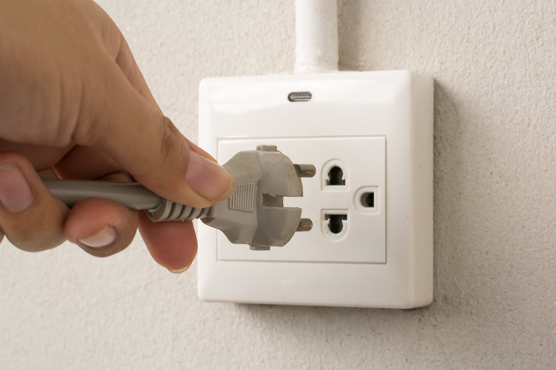 A hand about to plug a plug into an outlet