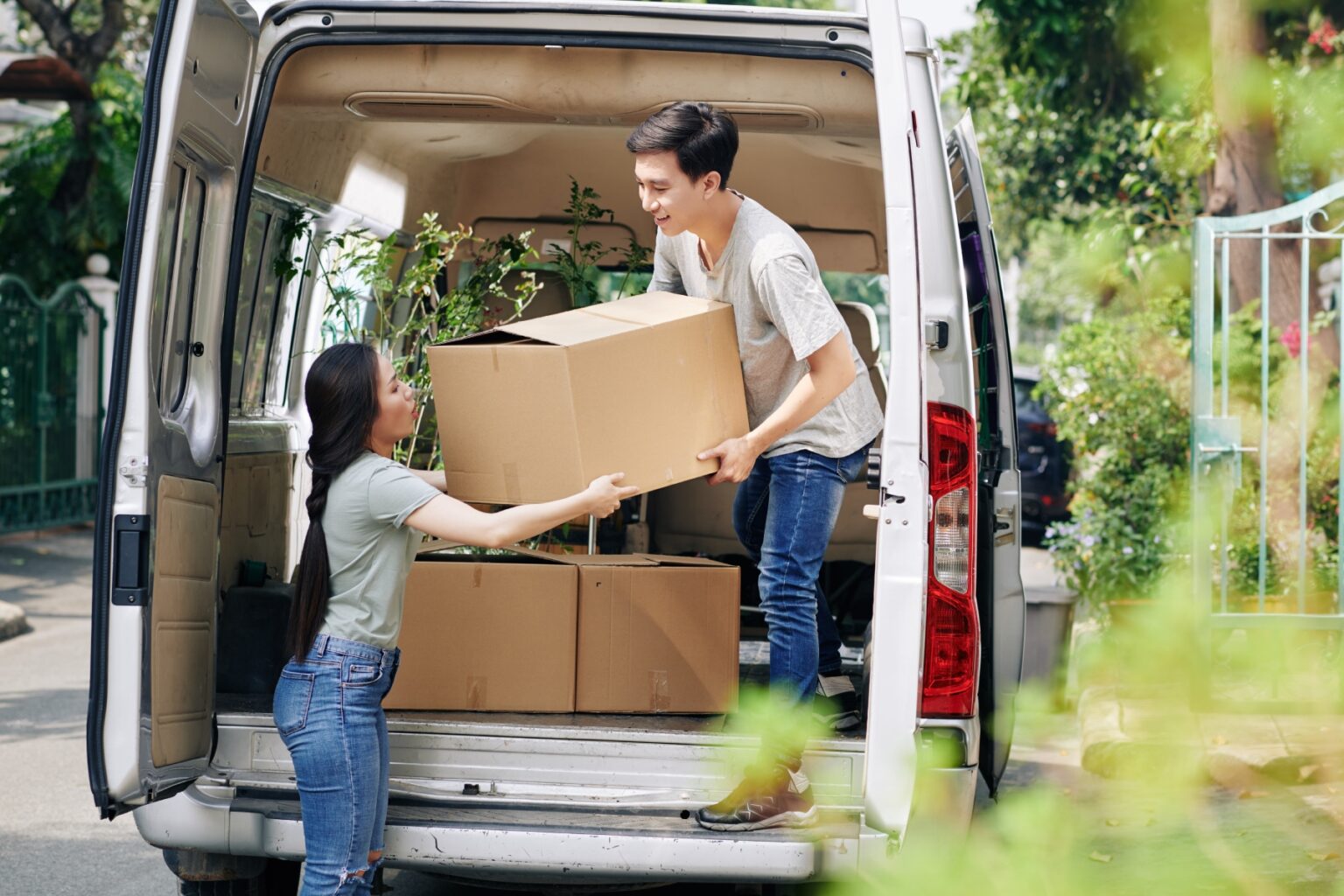 A man and a woman unload a box from a van filled with other boxes and plants