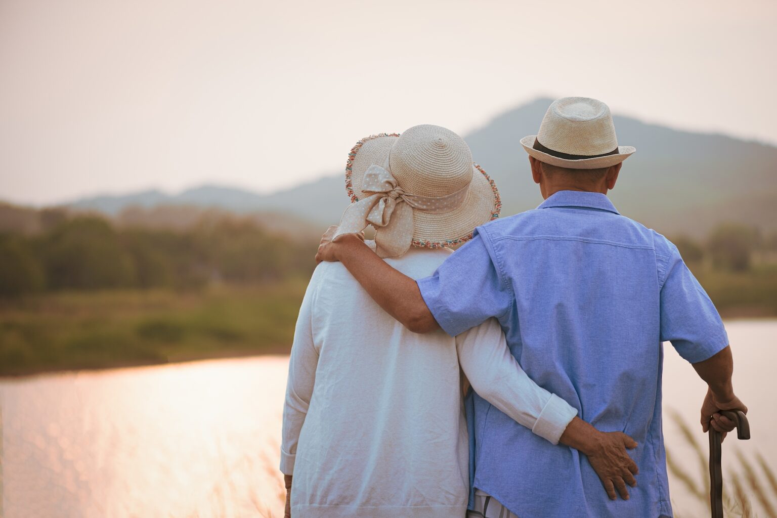 An older couple stands with arms around each other looking out over a natural landscape