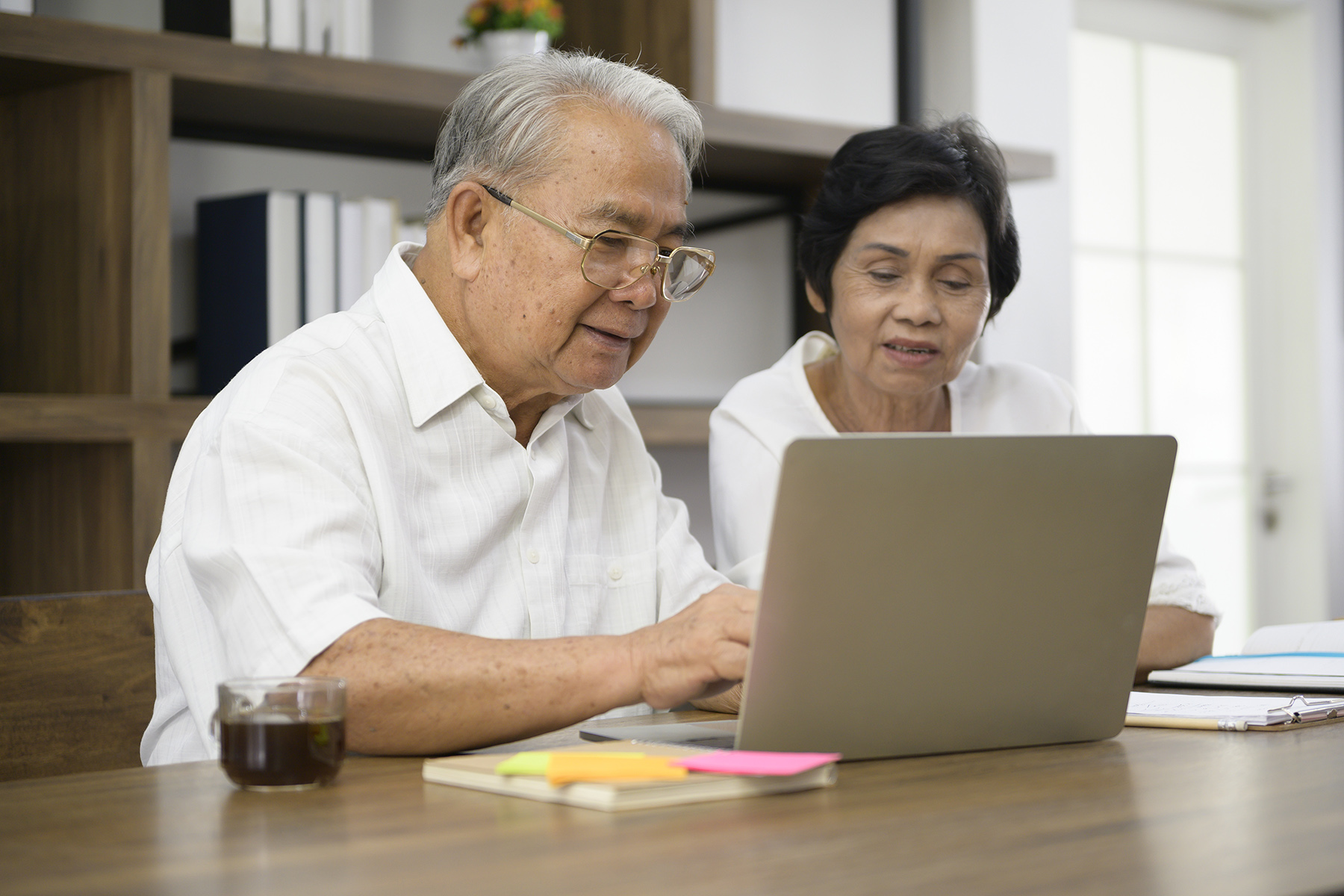 An older couple sit at a table while working on a laptop