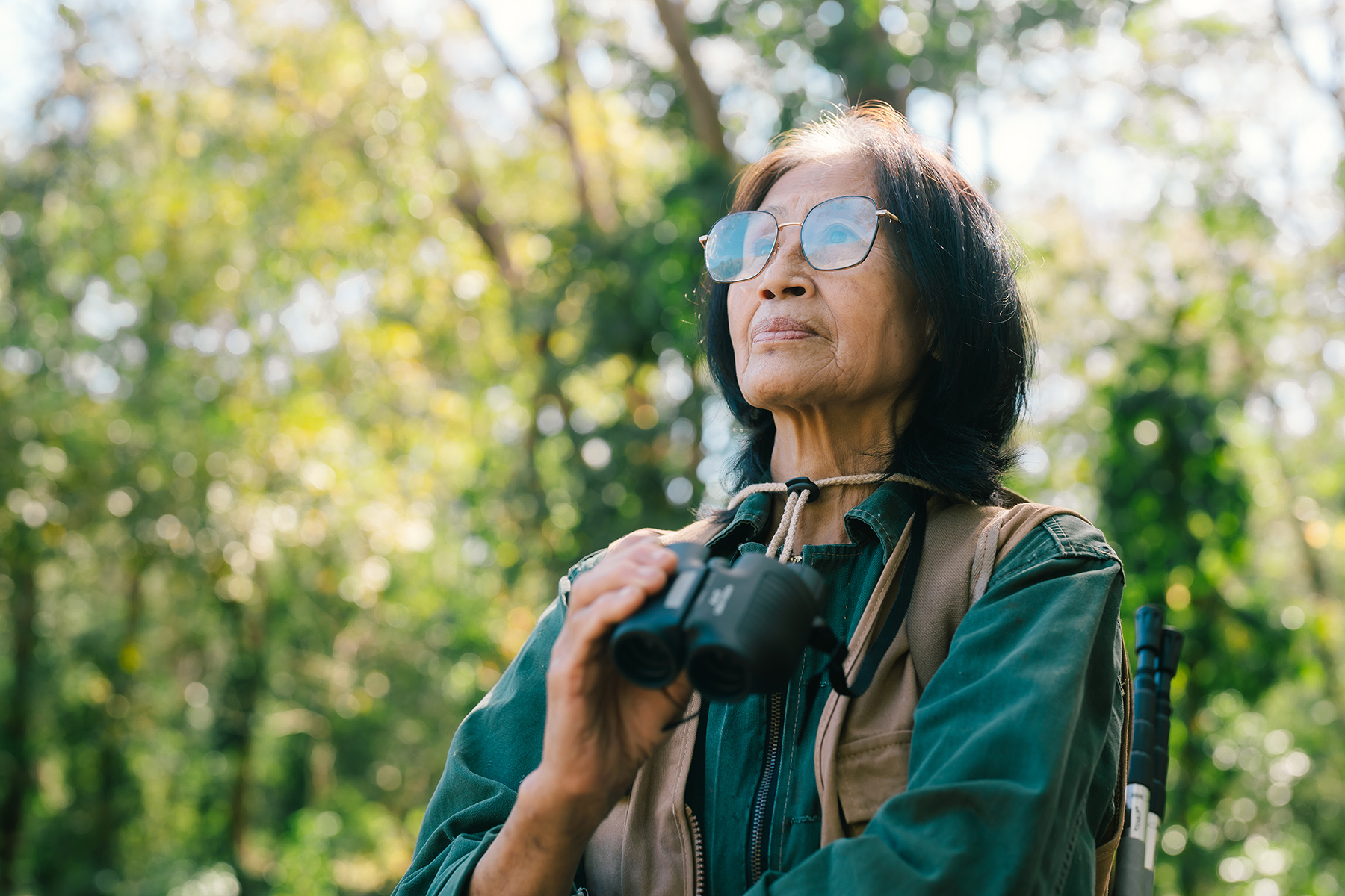 A retired woman in Thailand, with binoculars around her neck, enjoying the outdoors.  

