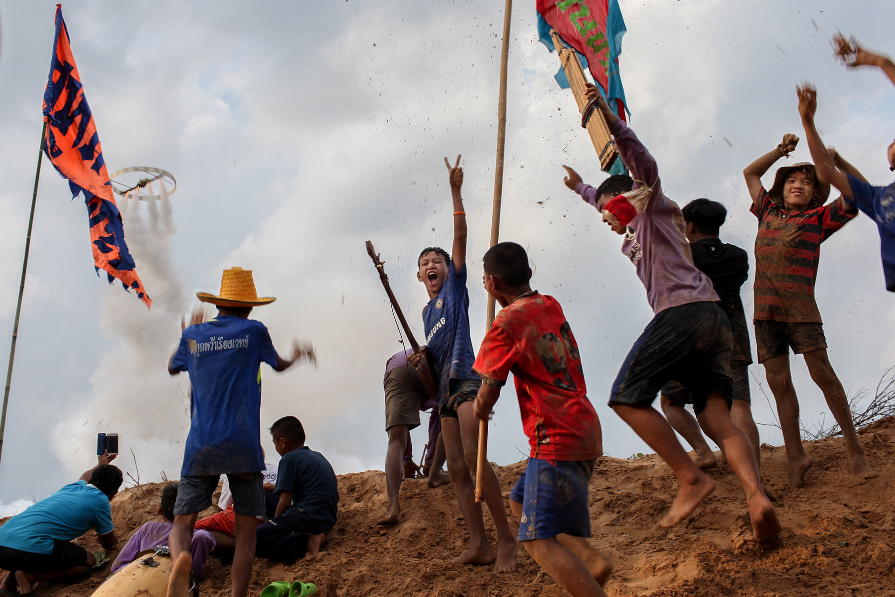 Young people jumping excitedly around a homemade rocket on a sand dune during the Bun Bang Fai Rocket Festival  in Thailand