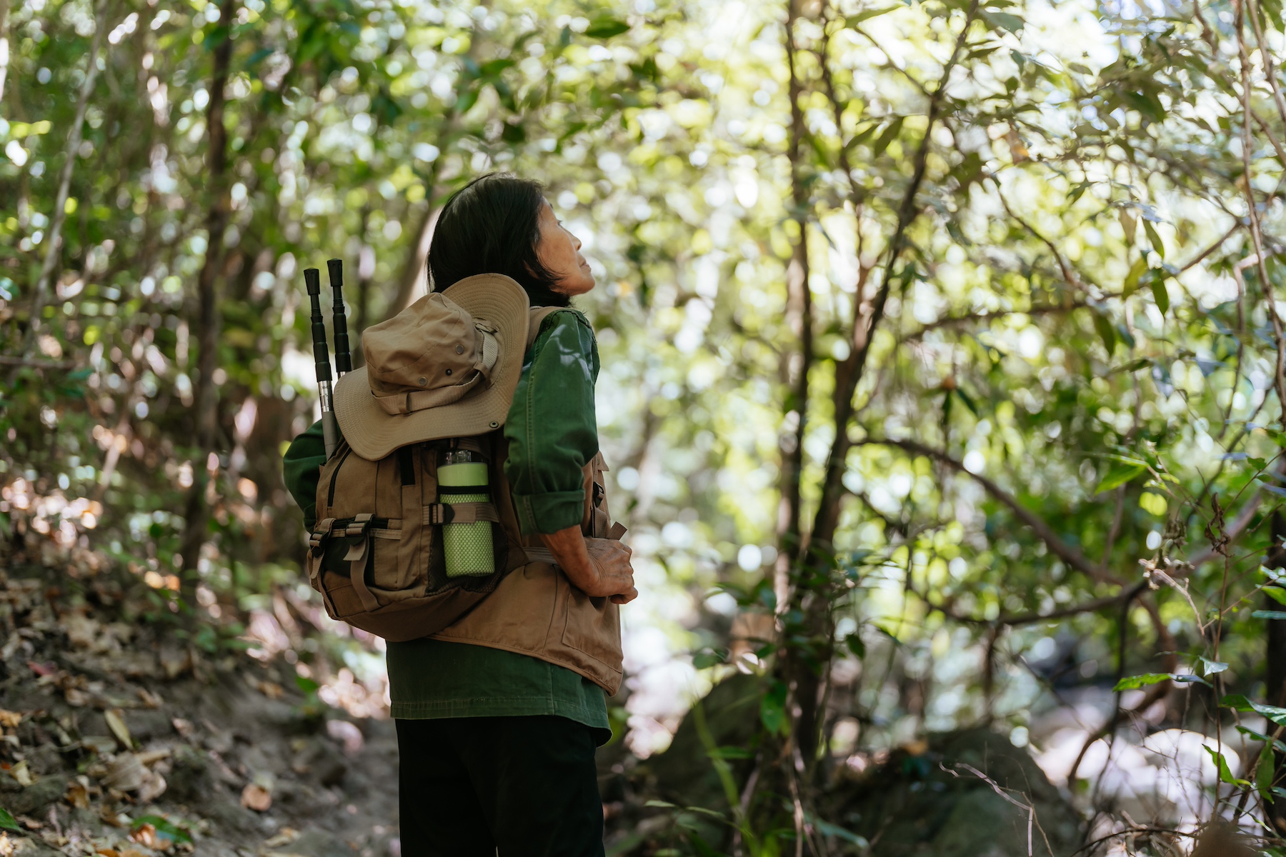 A woman in hiking gear stands alone looking around in the forest