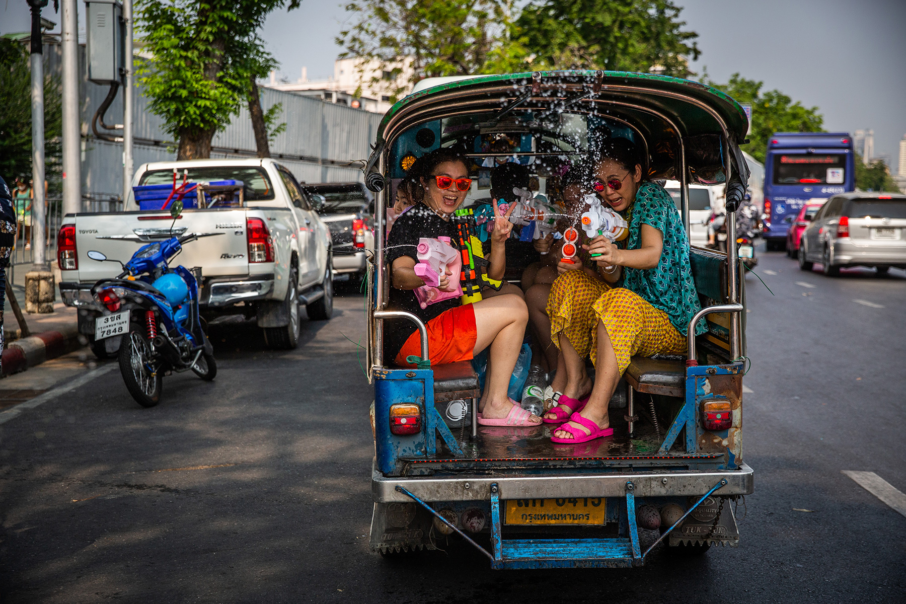 Two women spraying water guns from a traditional Thai truck, celebrating Songkran