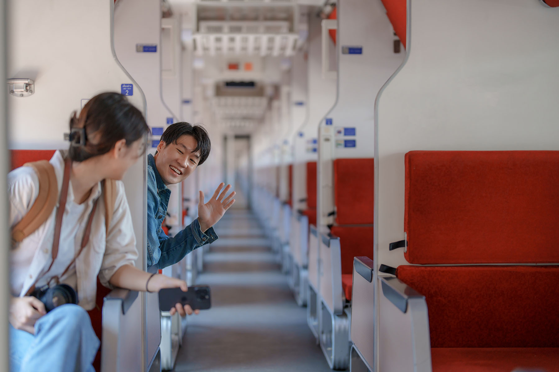 Man smiling and waving at a woman inside an empty train.