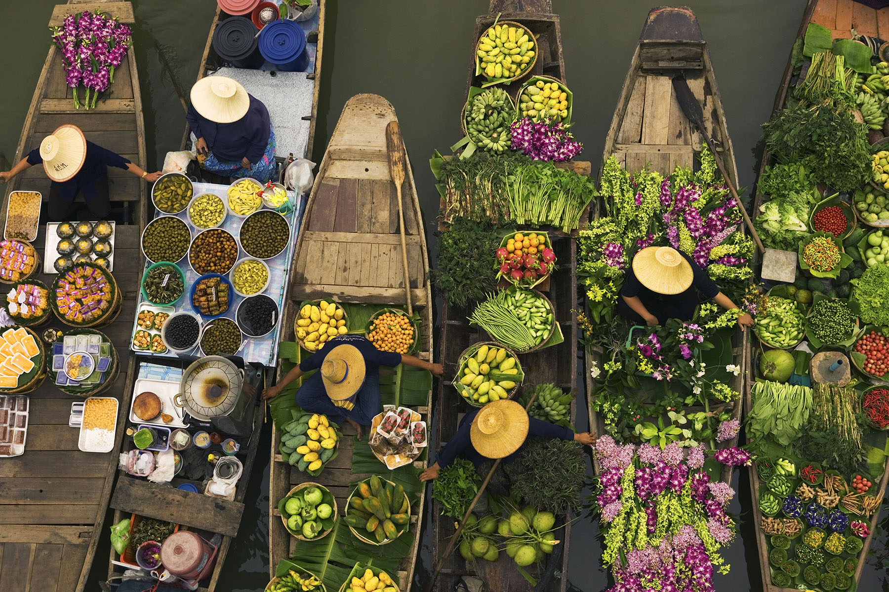 A floating market on a canal in Thailand, with boats laden with fresh produce, vegetables and fruit.