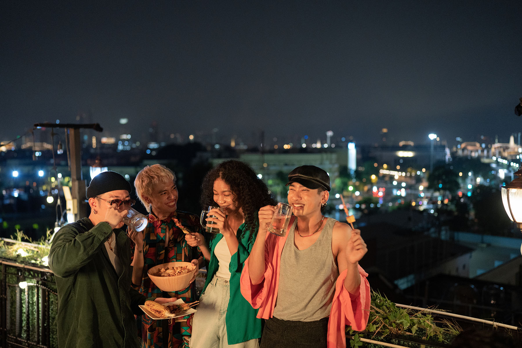 Group of lgbt+ friends hanging out on a rooftop, laughing, and enjoying snacks and drinks.