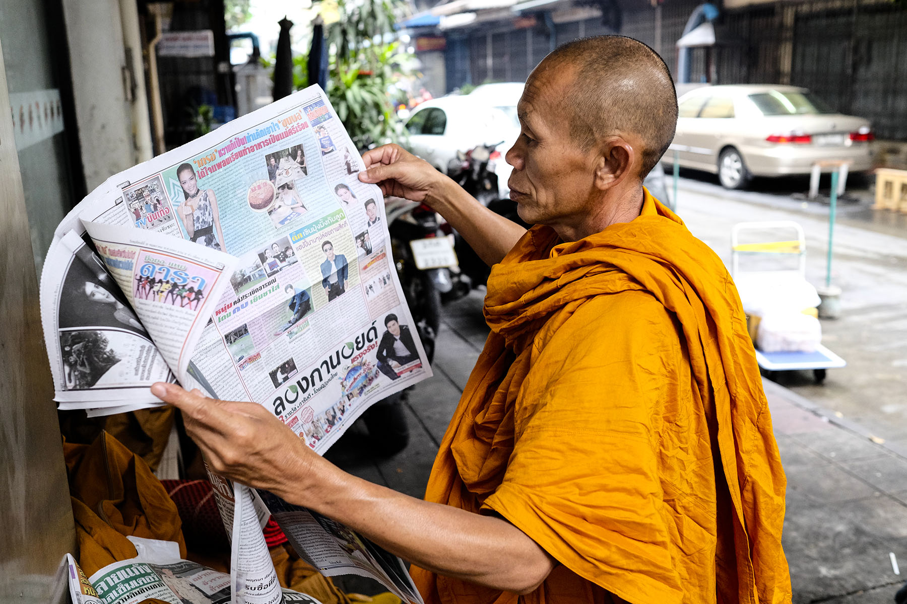 A Thai Buddhist monk reads a newspaper as he waits for others to join him during his morning walk.