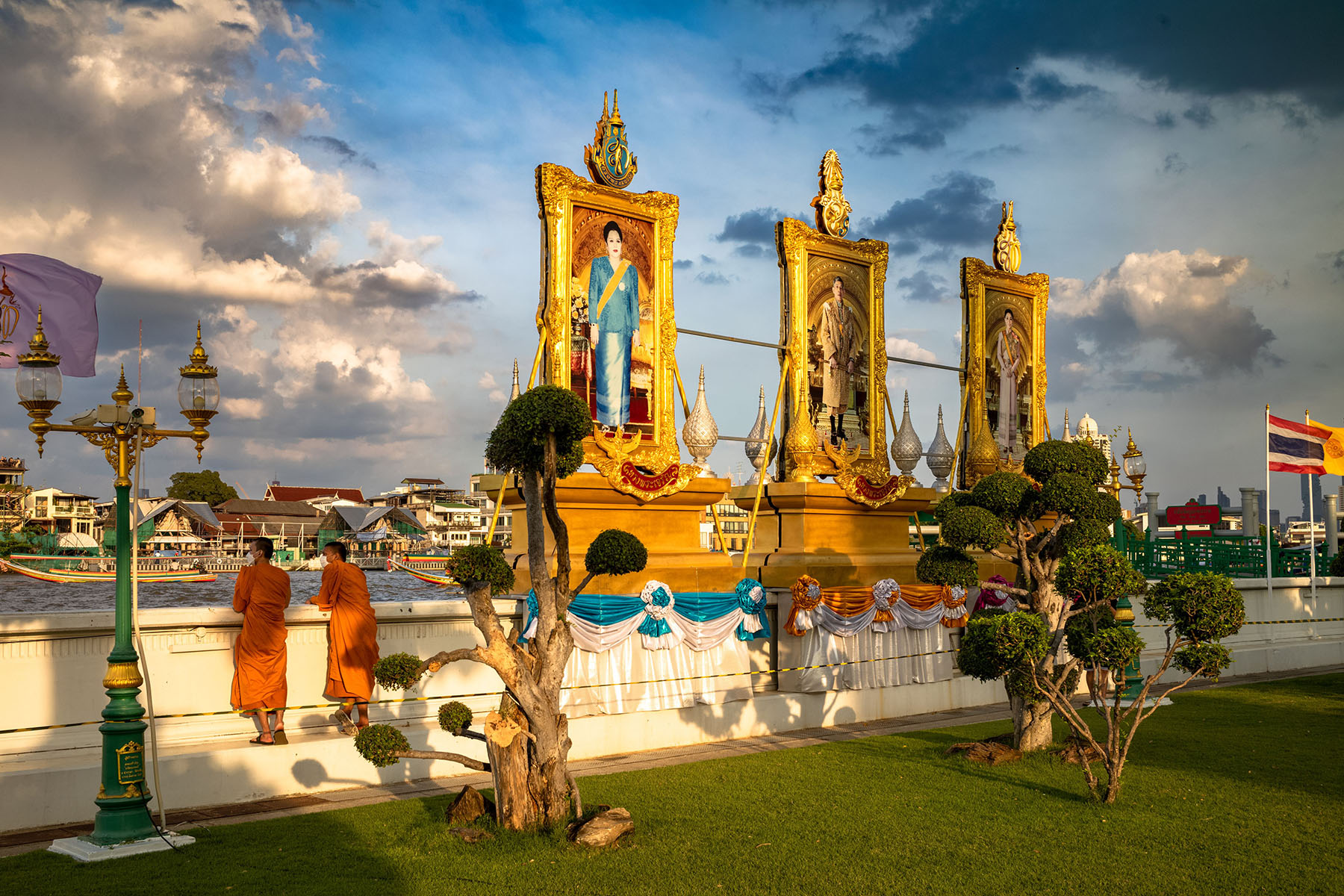 Two monks are overlooking the river while standing closeby three enormous royal portraits in Bangkok.