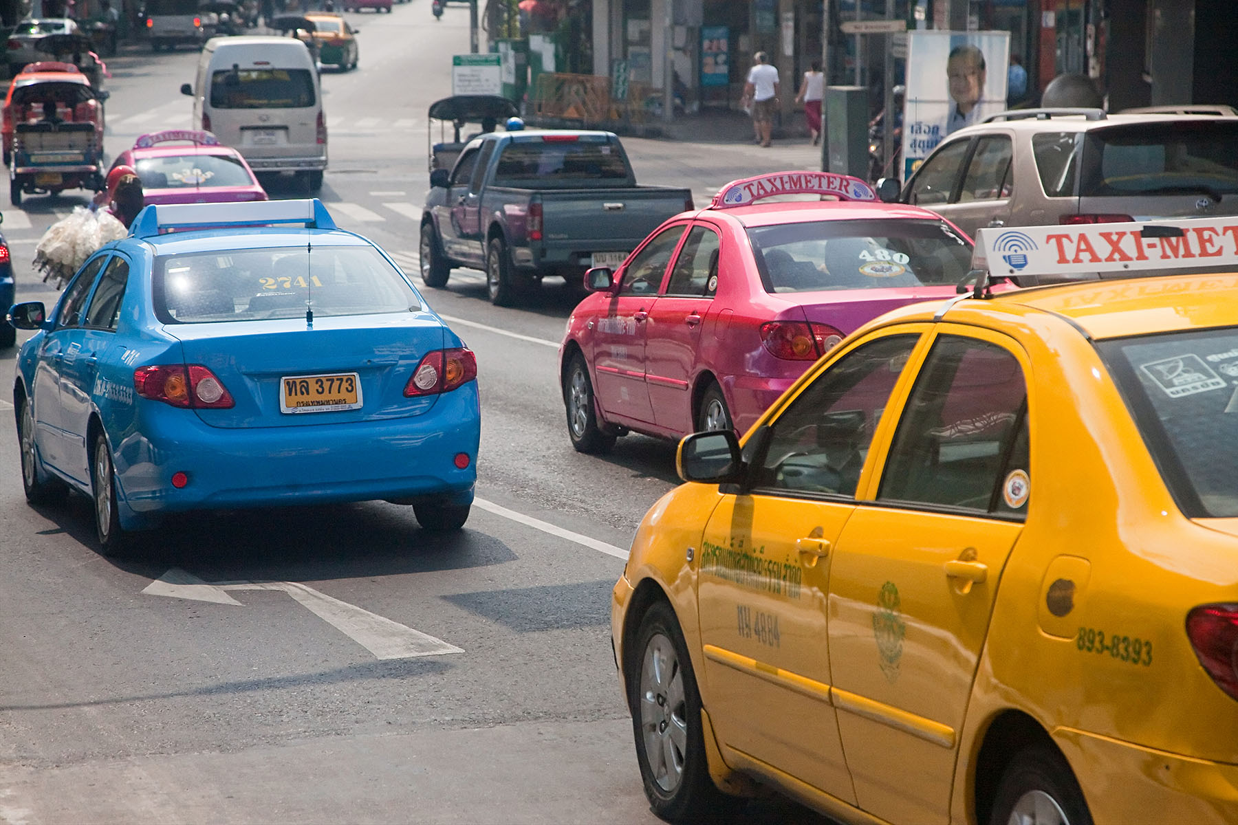 Different colored taxis driving through traffic in Bangkok.