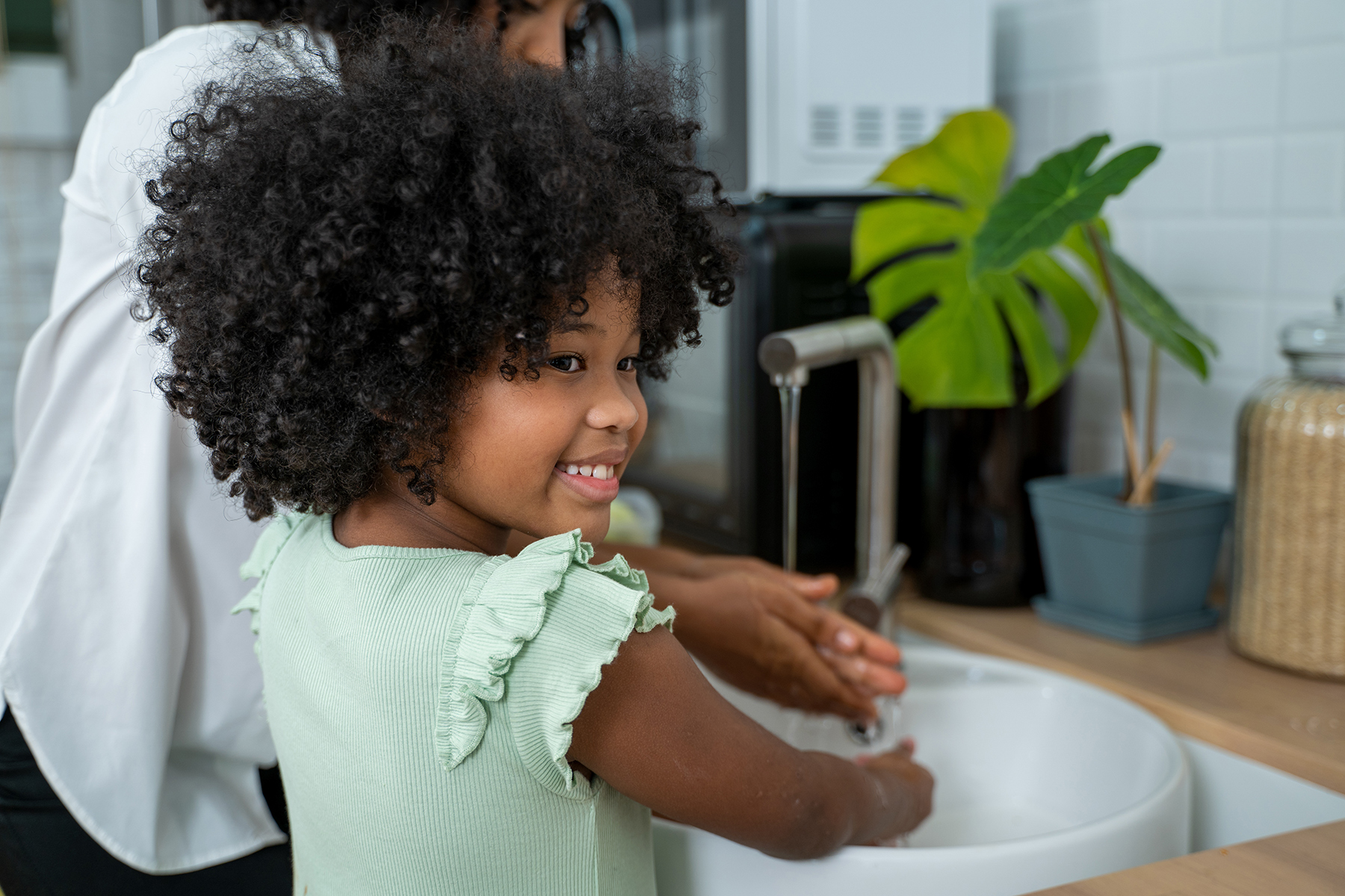 Girl and parent washing hands in sink