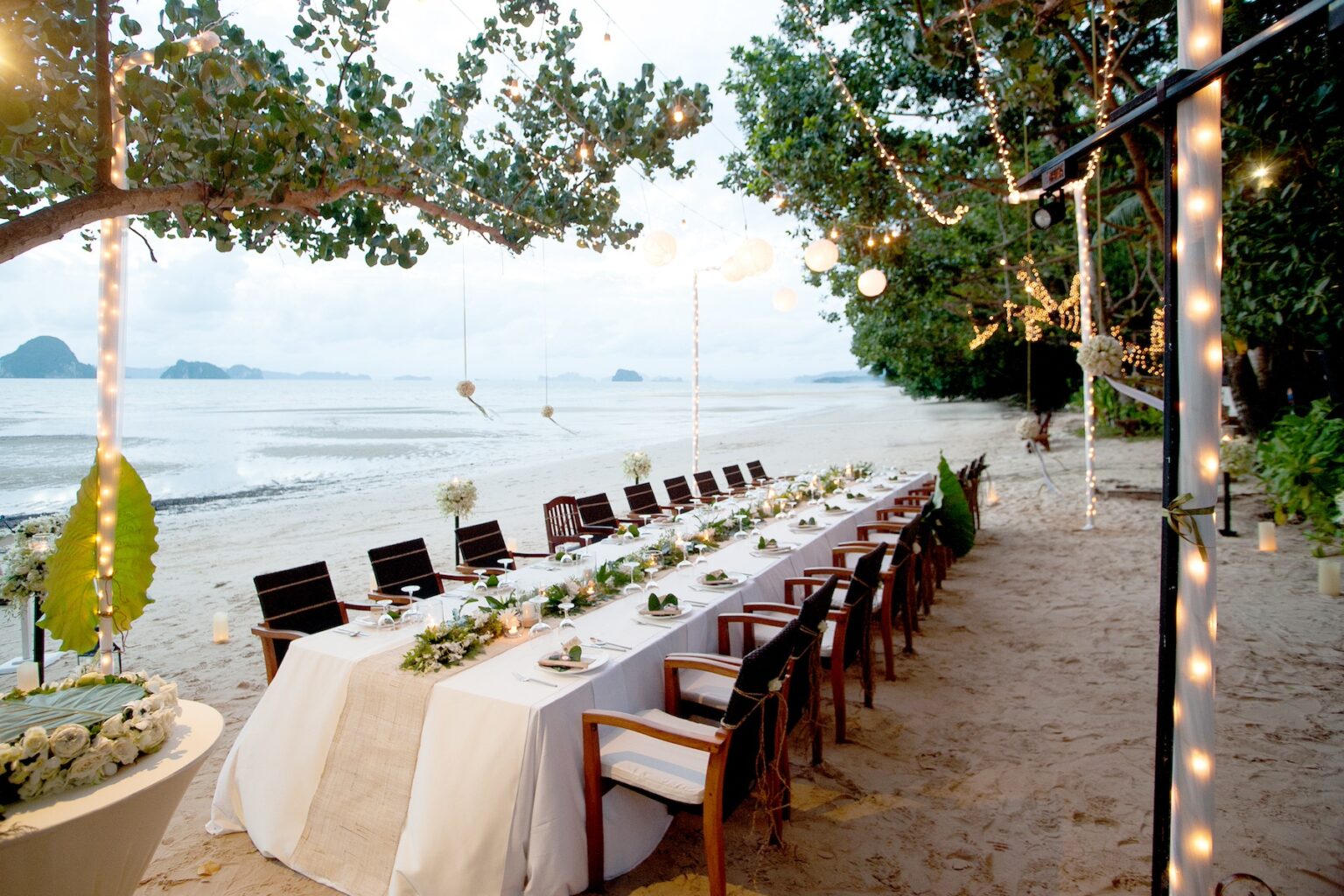 A beautiful long dining table with flowers and lights set up for a Thai beach wedding