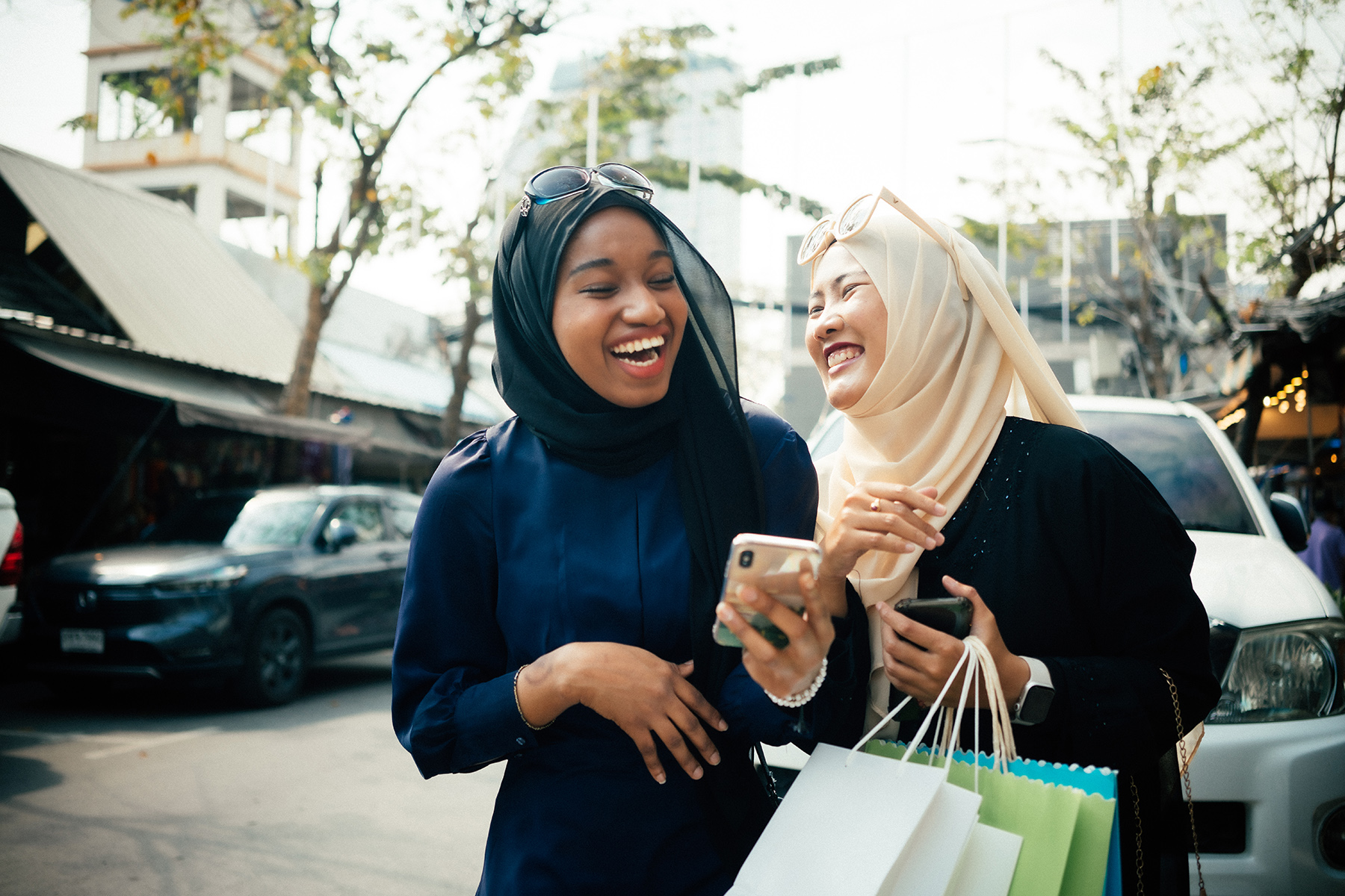 Two women chatting and laughing while holding their mobile phones and shopping


