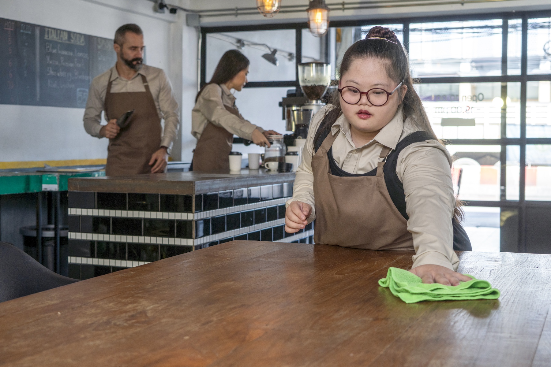 A young woman working as a barista cleans tables before the cafe opens for the day