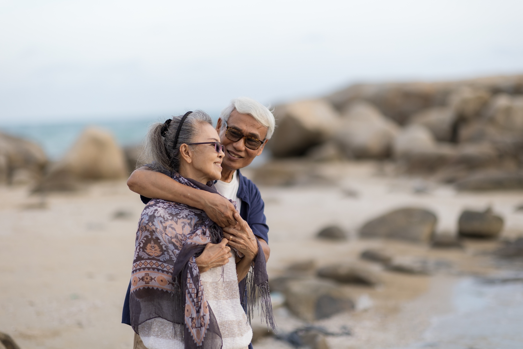 An older couple holds each other and smiles together on the beach