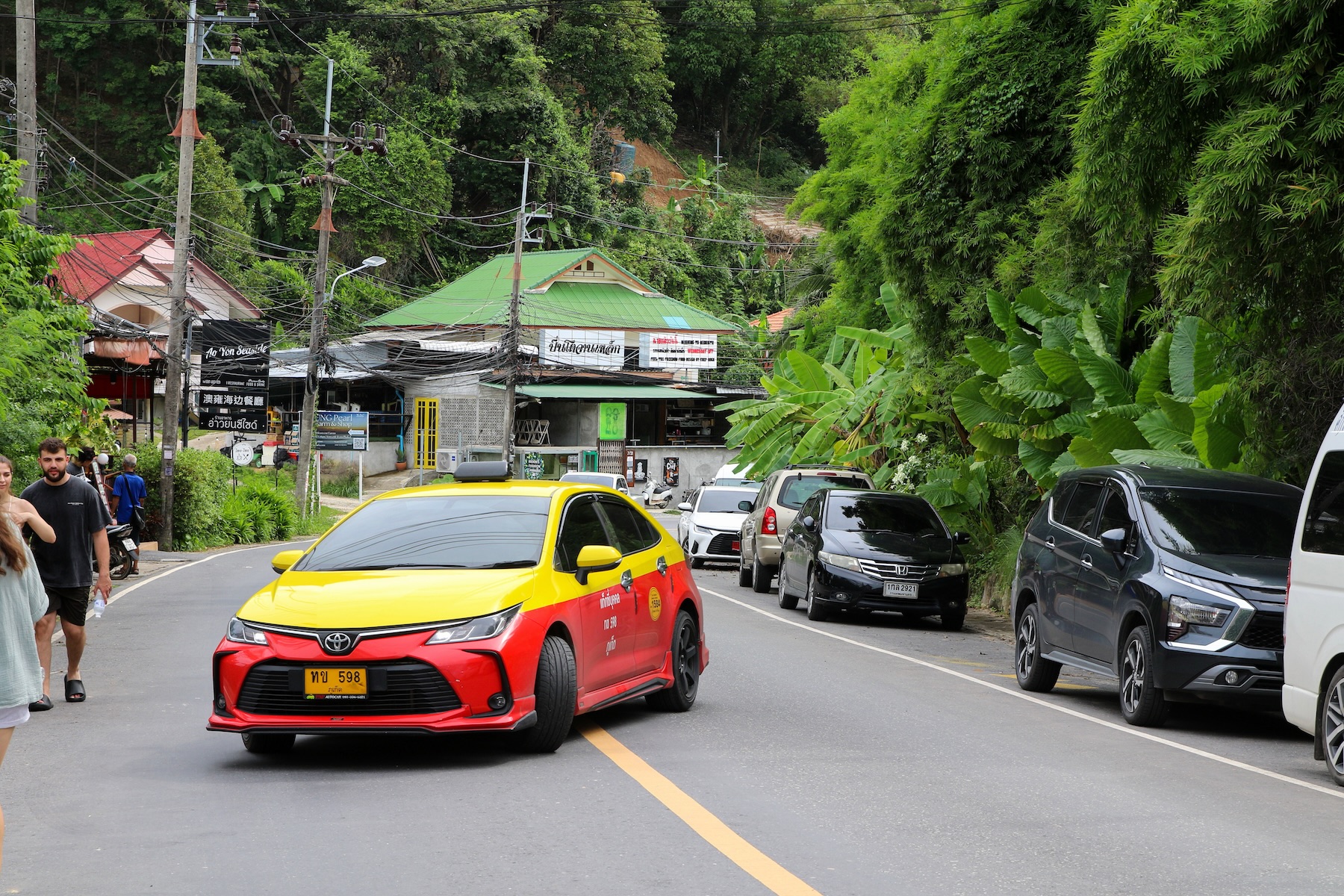 A taxi drives through the middle of a tree-lined mountain highway in Phuket, Thailand