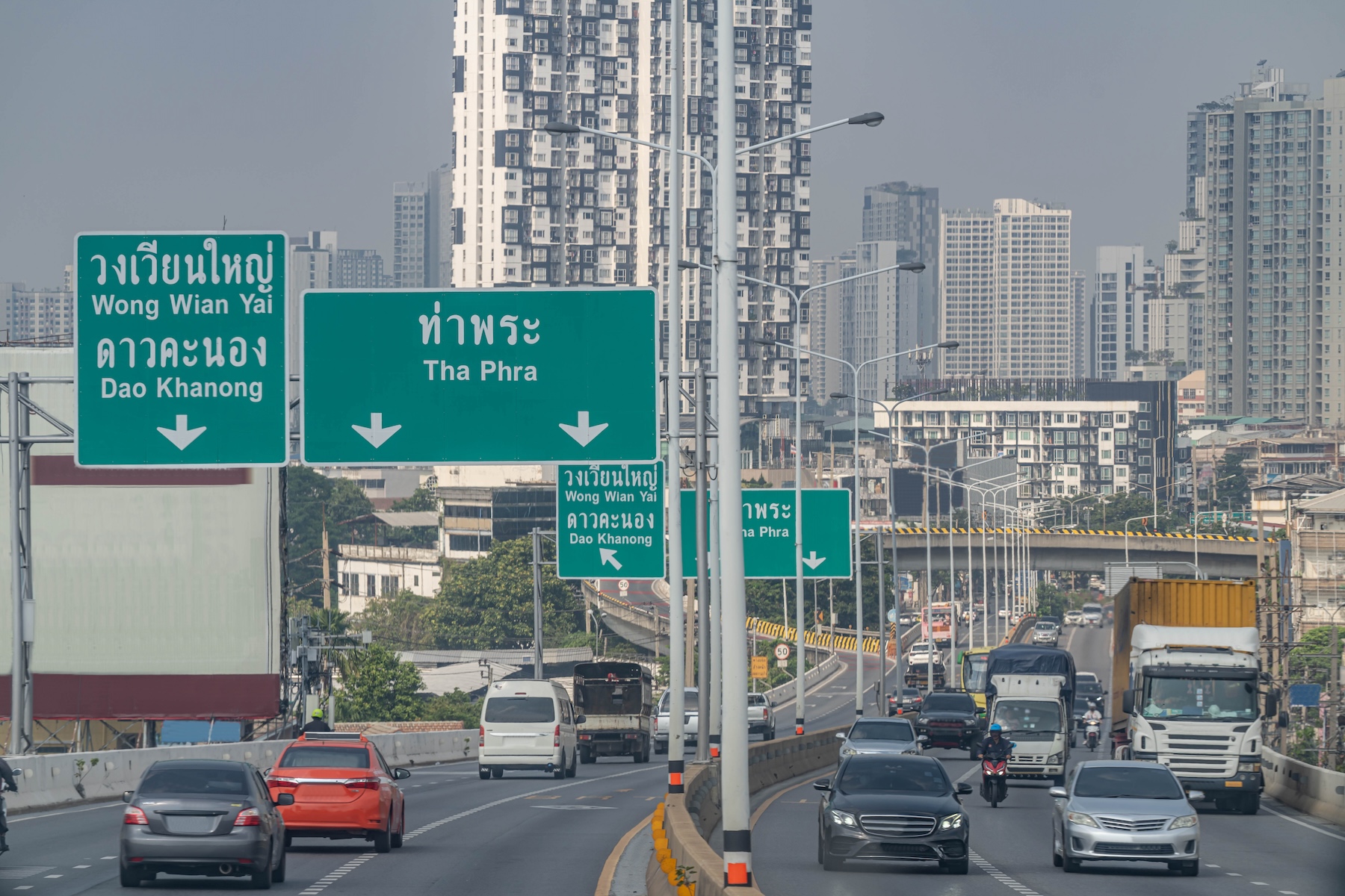 A busy road with signs and high-rise buildings in the Thon Buri district of Bangkok, Thailand
