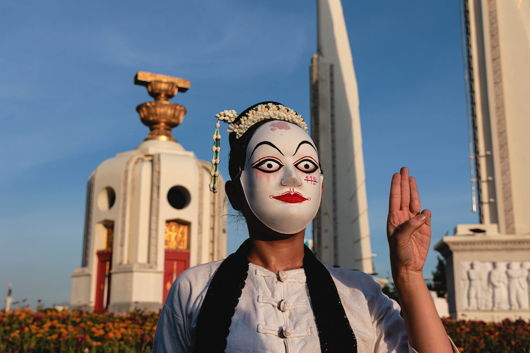 Protestor with a 'cursed mask' standing in front of the Democracy Monument in Bangkok. Their mask has 112 striped through, indicating their against the royal defamation law in Thailand.