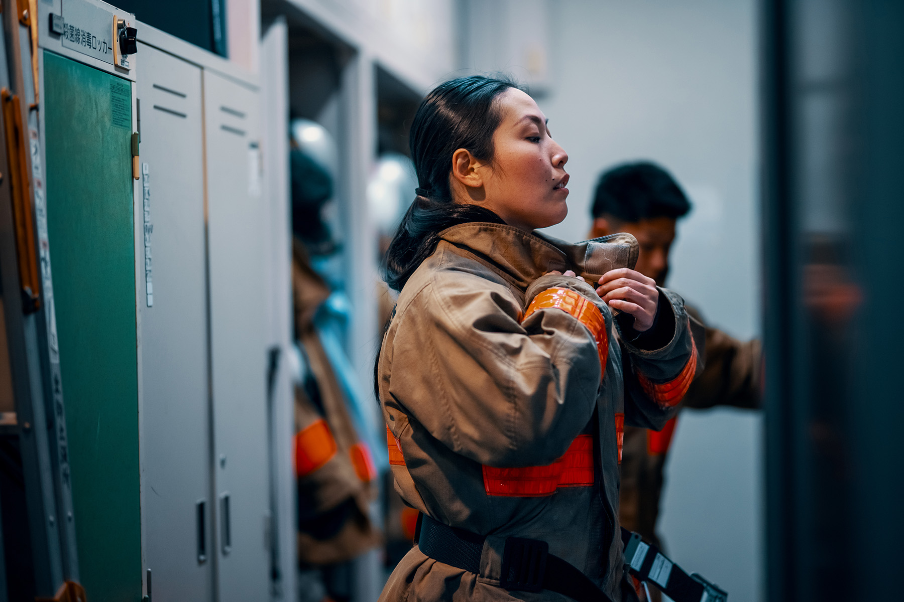 Female firefighter putting on her protective equipment at the fire station in response to an emergency.

