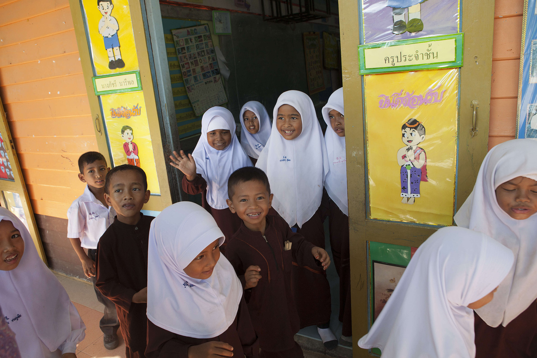 Elementary school children leaving class, some are smiling and waving at the camera.

